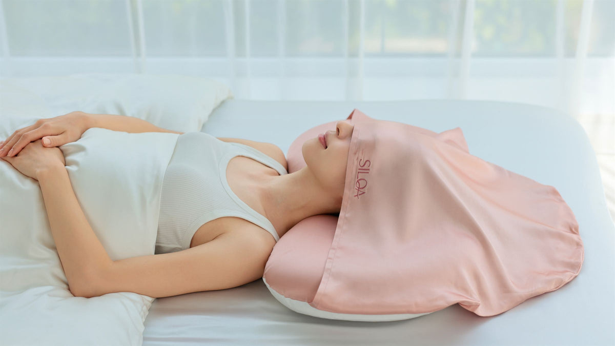 ピンクの生シルクフードをかぶってシルクセラムピローで眠る女性